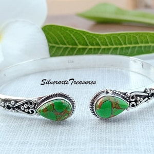 Pode incluir: Um bracelete de prata com duas pedras de turquesa verde engastadas em forma de lágrima. O bracelete é aberto e tem um design delicado.