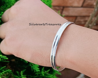 May include: A silver bangle bracelet with a smooth, polished finish. The bracelet is worn on a person's wrist.