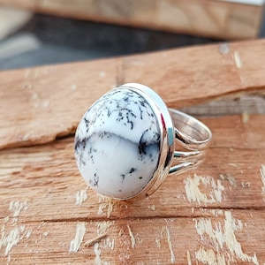 May include: A silver ring featuring a white and black dendritic agate stone. The stone displays a natural, organic pattern.