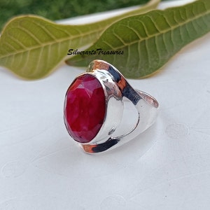 May include: A silver ring with a large, oval-shaped, red gemstone set in the center. The ring has a unique, open design with a curved band.