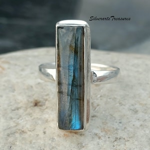 Può includere: Un anello d'argento con una pietra rettangolare di labradorite blu. L'anello è incastonato in una fascia semplice.