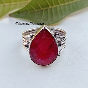 May include: A silver ring featuring a large, teardrop-shaped ruby gemstone. The ring has a delicate, twisted band with small accents.