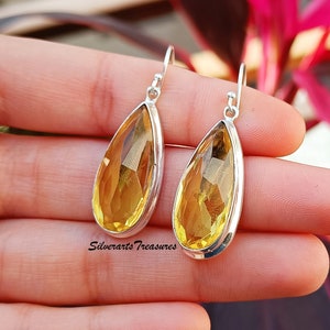 May include: A pair of silver teardrop earrings with yellow gemstones. The earrings have a simple design and are perfect for everyday wear.