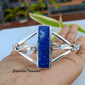 May include: A silver bracelet with a rectangular lapis lazuli stone set in the center. The bracelet has a delicate, intricate design with curved lines and small beads.