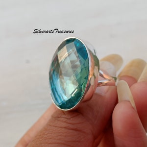 May include: A silver ring with a large, oval-shaped, faceted, blue-green gemstone. The ring is set in a silver band with a simple design.