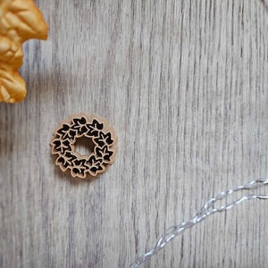 May include: A brown wooden wreath with a leaf design on a light wood background.