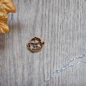 May include: A wooden cookie cutter shaped like a teapot with a mushroom on top. The cutter is brown and has a detailed design.