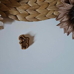May include: A brown plastic cookie cutter shaped like a witch with a pointed hat.