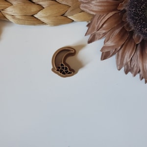May include: A brown crescent moon cookie cutter with a floral design.