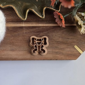 May include: A brown plastic cookie cutter shaped like a bow with a heart in the centre.