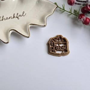 May include: A brown plastic cookie cutter shaped like a house with a chimney and windows.