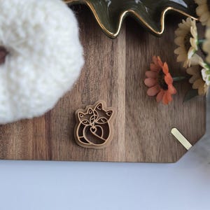 May include: A wooden cookie cutter in the shape of two cats cuddling. The cutter is brown and has a detailed design.