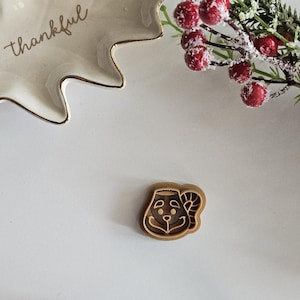 May include: A brown cookie cutter shaped like a gingerbread man with a smiling face. The cookie cutter is on a white surface.