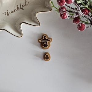 May include: Two wooden stamps, one shaped like a pagoda and the other shaped like a teardrop, on a white surface.