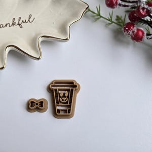 May include: Two brown plastic cookie cutters, one shaped like a cup of coffee with a smiling face and the other shaped like a bow tie.