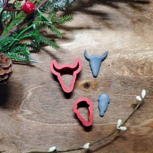 May include: A set of four cookie cutters in the shape of a bull's head, a buffalo skull, a cactus, and a cowboy boot. The cutters are made of red and gray plastic.