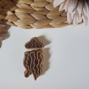 May include: A brown plastic cookie cutter shaped like a mushroom with a wavy stem.