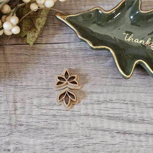 May include: Two brown, wooden cookie cutters shaped like flowers. The cutters are on a light brown wooden surface.