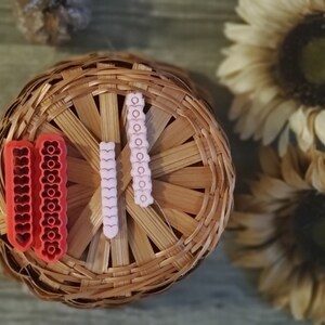 May include: Three sets of polymer clay earrings in a wicker basket. The earrings are shaped like hearts and are red, pink, and white.
