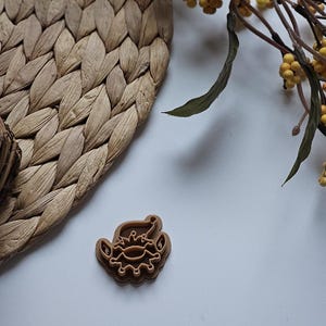 May include: A brown plastic cookie cutter shaped like a cartoon elf wearing a hat. The cookie cutter is on a white surface.