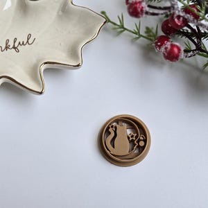 May include: A brown resin cookie cutter in the shape of a cat sitting on a crescent moon with stars.