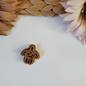 May include: A brown wooden turtle cookie cutter with a floral design. The cutter is on a white surface.