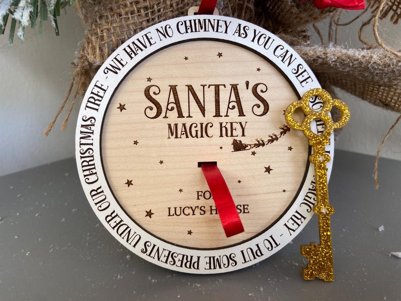 May include: A round wooden ornament with the text "Santa's Magic Key" and "To put some presents under our Christmas tree - we have no chimney as you can see so... for Lucy's house". A gold glitter key is attached to the ornament.