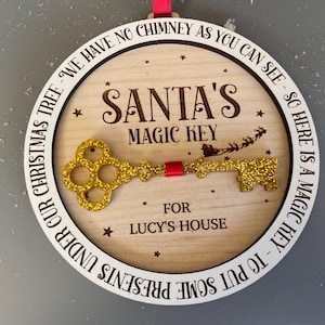 May include: A round wooden ornament with a gold glitter key and the text "SANTA'S MAGIC KEY" and "FOR LUCY'S HOUSE". The ornament is decorated with stars and the text "UNDER OUR CHRISTMAS TREE - WE HAVE NO CHIMNEY AS YOU CAN SEE - SO HERE IS A MAGIC KEY - TO PUT SOME PRESENTS".