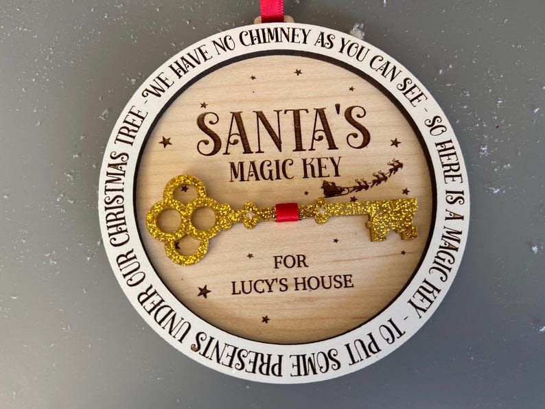 May include: A round wooden ornament with a gold glitter key and the text "SANTA'S MAGIC KEY" and "FOR LUCY'S HOUSE". The ornament is decorated with stars and the text "UNDER OUR CHRISTMAS TREE - WE HAVE NO CHIMNEY AS YOU CAN SEE - SO HERE IS A MAGIC KEY - TO PUT SOME PRESENTS".