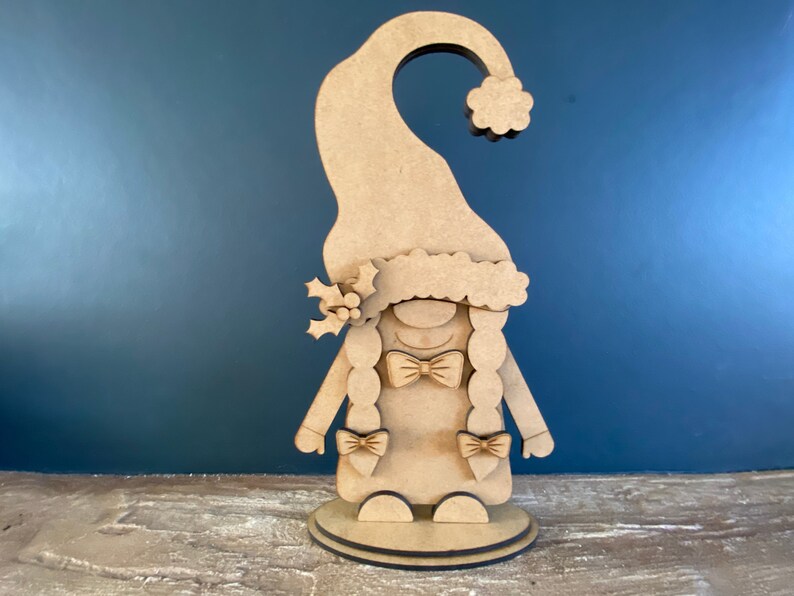 May include: A wooden gnome figurine with a red hat, a white fur trim, and a bow tie. The gnome is standing on a round base.