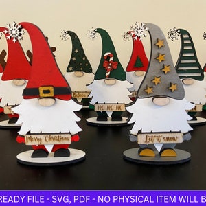 Puede incluir: Conjunto de nueve gnomos navideños de madera con sombreros de diferentes colores y letreros personalizados. Los letreros incluyen los nombres "Adam", "Believe", "Ho Ho Ho", "Merry Christmas", "Let it Snow" y "Say".