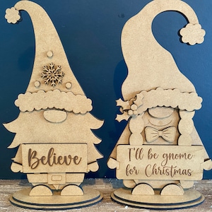 May include: Two wooden gnome figurines, one holding a sign that says "Believe" and the other holding a sign that says "I'll be gnome for Christmas".