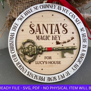 May include: A white wooden ornament with the text "Santa's Magic Key" and "For Lucy's House". The ornament also has a gold-colored key with a Santa figure on it.