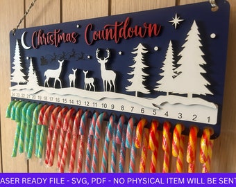 May include: A blue wooden Christmas countdown sign with a white deer, trees, and a crescent moon. The sign has 24 slots for candy canes, numbered 1-24. The text "Christmas Countdown" is written in red on the sign.