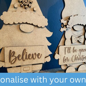May include: Two wooden Christmas gnomes, one holding a sign that says "Believe" and the other holding a sign that says "I'll be gnome for Christmas".