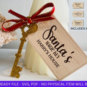 以下が含まれることがあります： 赤いリボンと「Santa's Magic Key, Harry's House」と書かれた木製タグが付いた、金のグリッターキー。画像には6つのタグデザインが含まれています。このキーはクリスマスの装飾品です。