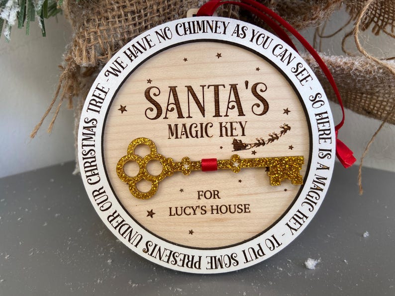 May include: A round wooden ornament with a white border and gold glitter key. The ornament reads "We have no chimney as you can see - so here is a magic key - to put some presents under our Christmas tree - Santa's Magic Key for Lucy's House".