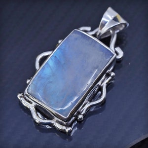 May include: A silver pendant with a large, rectangular, iridescent blue gemstone set in a silver frame. The frame has a decorative, swirling design.