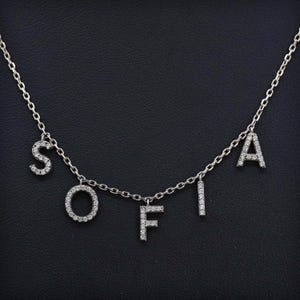 May include: A silver chain necklace with the name "SOFIA" spelled out in diamond-encrusted letters.