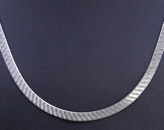 Puede incluir: Un collar de cadena plateada con diseño de espiga. El collar tiene un diseño plano y ancho con una superficie texturizada. La cadena se muestra sobre un fondo oscuro, resaltando su brillo metálico. Adecuado para diversas ocasiones.