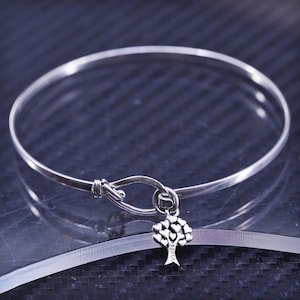 May include: A silver bangle bracelet with a heart-shaped tree charm. The charm is made of silver and has a small inscription on the bottom.