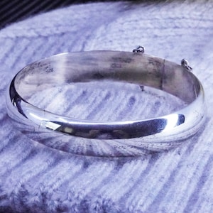 Peut inclure: Un bracelet jonc en argent avec une finition lisse et polie. Le bracelet est doté d'un fermoir à charnière et est marqué "925" à l'intérieur.