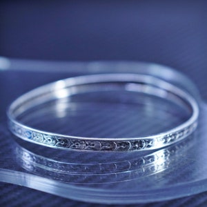 May include: A silver bangle bracelet with an intricate floral design.