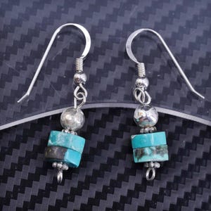 May include: A pair of silver dangle earrings with turquoise stones. The earrings have a silver hook and a silver bead above the turquoise stones.