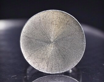 May include: A silver-colored, circular ring with a textured surface. The ring has a brushed metal appearance and a simple, minimalist design. The ring is likely made of stainless steel or a similar metal.