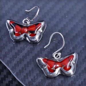 May include: A pair of silver butterfly earrings with red and black resin accents. The earrings are dangle style with a hook closure.