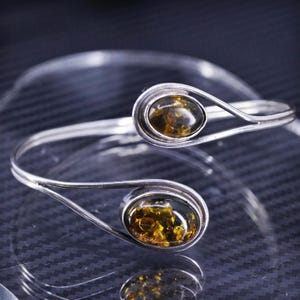 May include: A silver bangle bracelet with two amber stones. The bracelet is open and has a curved design.