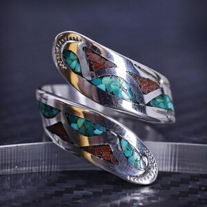May include: A silver ring with a turquoise and red stone inlay design. The ring is a wrap-around style and has a smooth, polished finish.