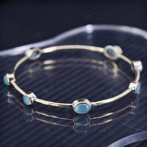 May include: A gold bangle bracelet with six light blue oval-shaped gemstones.