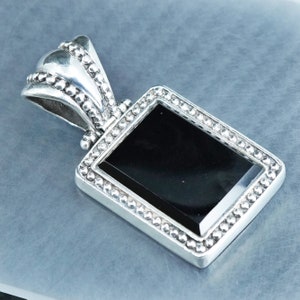May include: A silver pendant with a black onyx stone set in a beaded frame. The pendant has a detailed bail with a beaded design.